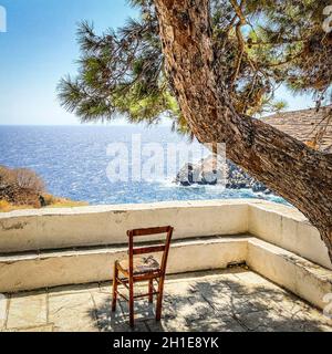 Leerer Stuhl auf der Terrasse vor dem ägäischen Meer unter dem Schatten von Kiefern, Insel Sifnos, Griechenland, Stockfoto