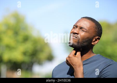 Mann mit schwarzer Haut, der Halsschmerzen leidet und an einem sonnigen Tag in einem Park steht Stockfoto