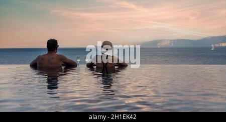 Pärchen genießen einen romantischen Blick auf das Meer und trinken Champagner im randlosen Pool im Luxus-Resort. Banner-Kopierfläche Stockfoto