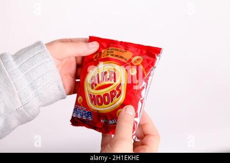 Ungeöffnetes Paket mit Hula Hoops in jungen Händen vor weißem Hintergrund Stockfoto