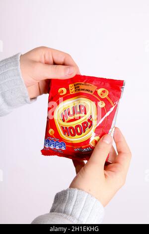 Ungeöffnetes Paket mit Hula Hoops in jungen Händen vor weißem Hintergrund Stockfoto