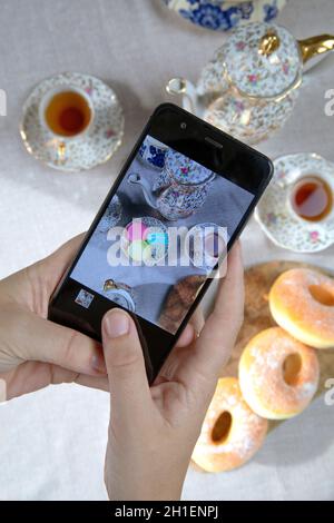 Draufsicht Bild der Dame, Blogger sitzen im Café und machen Foto mit Mobile von Lebensmitteln, Nachmittagstee mit Donuts und Makronen auf dem Tisch hoch Stockfoto