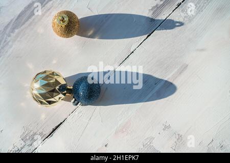 Glitzernde goldene und dunkelblaue weihnachtskugeln auf weißem Holzhintergrund im Sonnenlicht Stockfoto