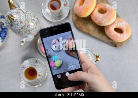 Draufsicht Bild der Dame, Blogger sitzen im Café und machen Foto mit Mobile von Lebensmitteln, Nachmittagstee mit Donuts und Makronen auf dem Tisch hoch Stockfoto