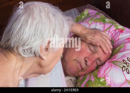 Älterer, über 80-jähriger Mann in einem Heimbett und seine Frau. Krankheit, Altern, ungesunde Konzepte Stockfoto