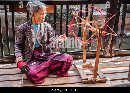 INLE LAKE, MYANMAR - 8. JANUAR 2014: Burmesische Frau spinnt Garn in der Weberei, in der Textilien auf traditionelle Weise hergestellt werden Stockfoto