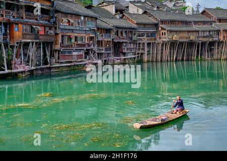 FENGHUANG, CHINA - 23. APRIL 2018: Nicht identifizierter chinese im Boot Feng Huang Ancient Town (alte Stadt Phoenix) auf dem Tuo Jiang Fluss mit Brücke und Stockfoto