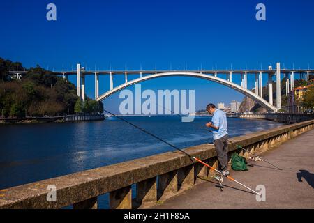 Porto, PORTUGAL - MAI 2018: Mann, der in der Nähe der Flussmünde des Douro und der Arrabida-Brücke in einem schönen frühen Frühlingstag in Porto City im Portu fischt Stockfoto
