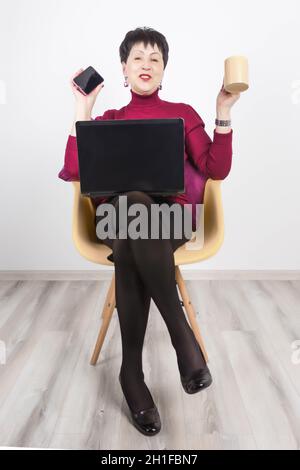 Ältere Frau mit Laptop und Mobiltelefon auf grauem Studiohintergrund. Stockfoto