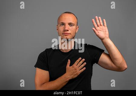 Ich verspreche, die Wahrheit zu sagen. Porträt eines ehrlichen verantwortungsbewussten Mannes in einem schwarzen Hemd mit einer Hand auf dem Herzen und der anderen, der einen Eid ablegte, der sich verpflichtete Stockfoto