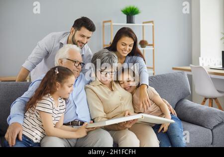 Glückliche Großeltern der Familie mit ihren Zwillingstöchtern und ihren Eltern stöbern im Familienfotoalbum. Stockfoto