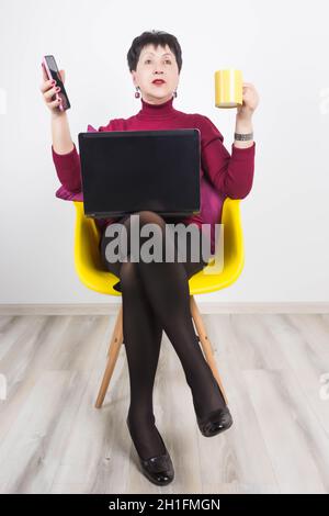 Ältere Frau mit Laptop und Mobiltelefon auf grauem Studiohintergrund. Stockfoto