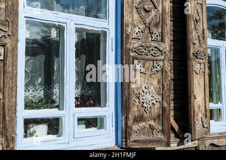 Detail des traditionellen Holzhauses mit blauem Fenster und braun geschnitzten Fensterläden in Ulan-Ude. Republik Burjatien, Russland Stockfoto