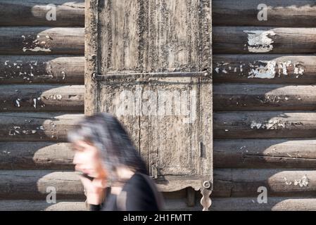 Verschwommene Frau, die an einem der traditionellen Holzhäuser in Ulan-Ude entlang geht. Republik Burjatien, Russland Stockfoto