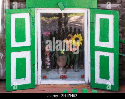 Künstliche Blumen hinter einem Fenster mit grünen Fensterläden eines traditionellen Holzhauses in Ulan-Ude. Republik Burjatien, Russland Stockfoto