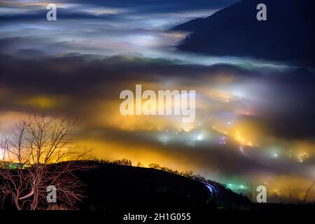 Blick von oben auf den dichten Nebel, der von den Nachtlichtern der Dörfer, der Po-Ebene, Provinz Vicenza, Italien, gefärbt wird Stockfoto