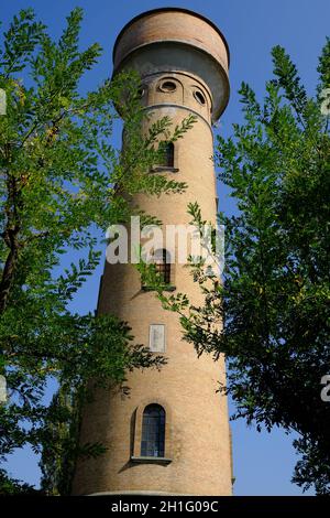 Der zylindrische Ziegelturm ragt in den blauen Himmel. Aquädukt-Turm mit Bogenfenstern, aus Terrakottafliesen gebaut und von hohen Pappelbäumen umgeben. Stockfoto