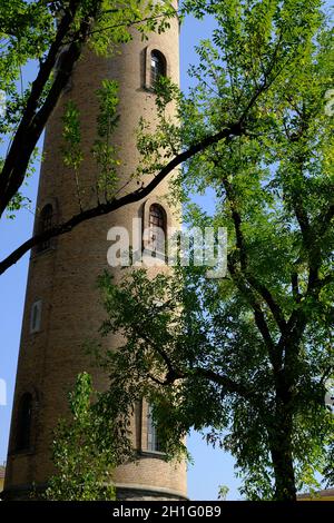 Der zylindrische Ziegelturm ragt in den blauen Himmel. Aquädukt-Turm mit Bogenfenstern, aus Terrakottafliesen gebaut und von hohen Pappelbäumen umgeben. Stockfoto