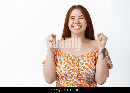 Ja, sie hat es getan. Ehrgeiziges junges Rotschopf-Mädchen, das smeth gewann, lächelte und vor Freude sprang, das Ziel erreicht, auf weißem Hintergrund stand Stockfoto