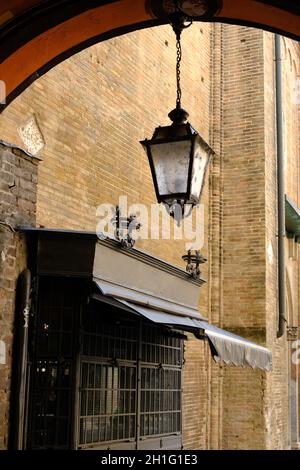 Fensterläden und Laterne aus Schmiedeeisen. Roter Backsteinbogen im historischen Zentrum der Stadt. Lodi, Lombardei, Italien. Stockfoto