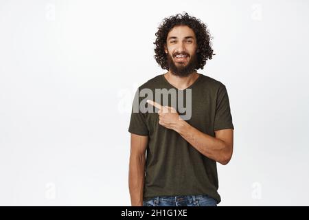 Porträt eines lächelnden arabischen Mannes, der nach links zeigt, Werbung zur Seite zeigt und in T-Shirt auf weißem Hintergrund steht Stockfoto