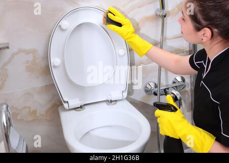 Eine Frau in einer Putzuniform wäscht die Toilette.Ich hob den Deckel auf der Toilette. Der Mann ist außer Fokus.Reinigungsservice im Hotel oder in ho Stockfoto
