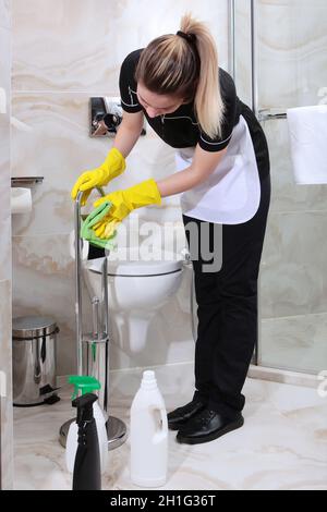 Ein Mädchen in einem Reinigungsservice-Anzug wischt sich einen Toilettenpapierständer ab. Sauberkeit und Hygiene im Bad. Speicherplatz kopieren. Stockfoto