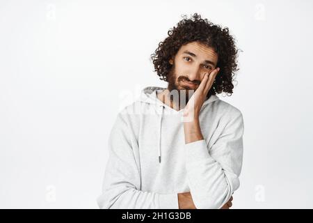Porträt eines jungen arabischen Mannes, der müde und verärgert aussieht, sich von etwas gelangweilt, den Kopf an der Hand lehnt und unamüsiert starrt, auf weißem Hintergrund stehend Stockfoto