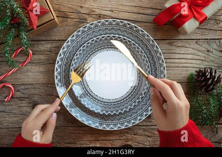 Frauenhand in rotem Strickpullover auf kreativem weihnachtstisch. Leere Teller auf rustikalem Holz Weihnachten Hintergrund. Stockfoto