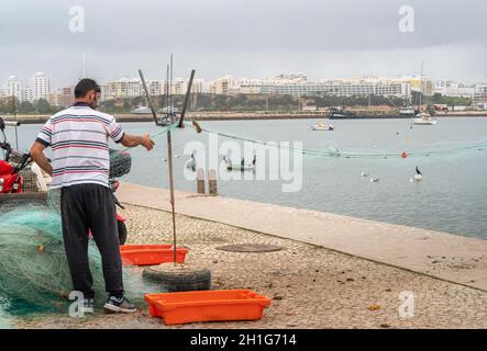 Fiisherman im Hafen, der Fische aus seinem Netz entfernt, Ferragudo an der Algarve, Portugal Stockfoto