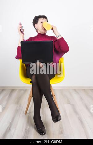 Ältere Frau mit Laptop und Mobiltelefon auf grauem Studiohintergrund. Stockfoto