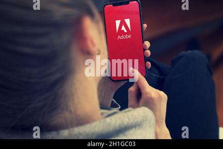KIEW, UKRAINE-JANUAR, 2020: Adobe auf Smartphone-Bildschirm. Junges Mädchen, das während einer pandemischen Selbstisolation und eines Coronavirus auf das Mobiltelefon zeigt oder es textet Stockfoto