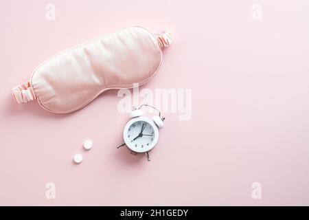 Schlafende Augenmaske, Wecker, Pillen auf rosa Hintergrund. Konzept zur Behandlung von Schlaflosigkeit. Stockfoto