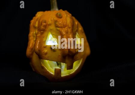 Glühender kleiner Halloween Kürbis auf schwarzem Hintergrund. Weit lächelnder Jack O Laterne halloween Kürbis mit Licht im Inneren. Furchterregend geschnitzter Kürbis. Stockfoto
