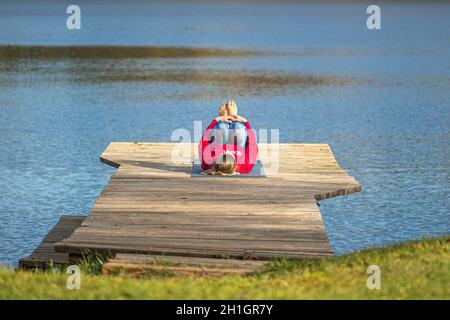 Schöne blonde Haare Mädchen Yoga zu tun und auf einem hölzernen Pier auf dem See im Herbst mit Wald auf dem Hintergrund liegen Stockfoto