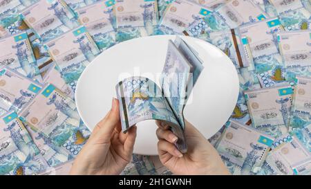 Zählen Sie Geld in Tenge. Viele kasachische Tenge auf einem weißen Teller. Die nationale Währung von Kasachstan. Gehalt in Tenge. Um das Budget zu kürzen. Stockfoto