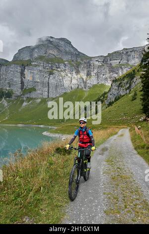 Die Biker-Frau fährt auf Einer unbefestigten Straße auf die Fotografin zu. Im Hintergrund Ein Wasserreservoir, Schafweiden und Berge. Sursel Stockfoto