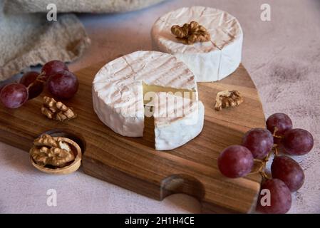 Käse mit weißem Schimmel, Trauben und Walnüssen auf einem Holzschneidebrett auf einer leichten Arbeitsplatte. Stockfoto