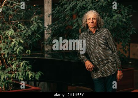 Porträt des 65-jährigen reifen Mannes am Klavier-Musikinstrument in der Lobby des Hotels grau lockiges Haar, charismatische Erscheinung. Stockfoto