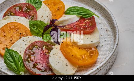 Macro Caprese Salat mit roten und gelben Tomaten, frischem Basilikum und Mozzarella Käse in Keramikplatte, selektiver Fokus Stockfoto