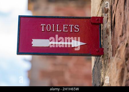 Toiletten, meine Damen, öffentliche Einrichtungen, Toiletten-Toilettensitze, Metallschilder, Gussmetall, alter Stil, roter Hintergrund. Hinweisschilder, Öffentlichkeit. Stockfoto