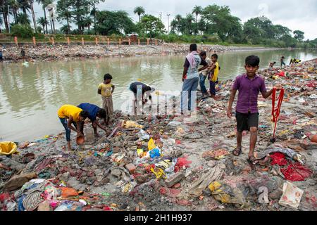 Muradnagar, Indien. Oktober 2021. Die Einheimischen und ihre Kinder sieben Wertgegenstände aus den Stapeln am Ufer des Ganges-Kanals in Muradnagar. Im Oberen Ganges-Kanal, der von schweren Bächen am Ufer des Kanals angehäuft wird, suchen die Dorfbewohner gerne nach wertvollen Gegenständen. Eifrige Anhänger bieten während eines Tauchgangs im Ganga-Kanal Wertsachen als religiöse Praxis an oder verlieren sie dort unwissentlich. Kredit: SOPA Images Limited/Alamy Live Nachrichten Stockfoto