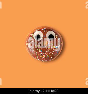 Halloween Donut mit schönen Augen auf orangefarbenem Hintergrund. Witziges Minimalkonzept. Stockfoto