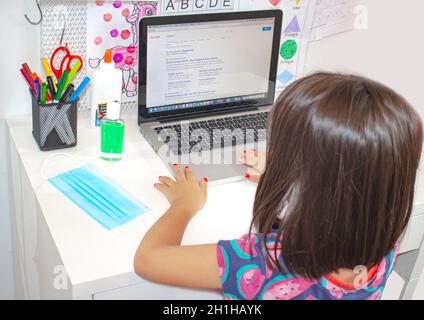 Calgary, Alberta, Kanada. September 2020. Ein Grundschüler, der einen Computermonitor mit Gesichtsmaske und Händedesinfektionsmittel auf einem Schreibtisch betrachtet. Stockfoto