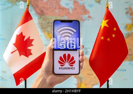 Calgary, Alberta, Kanada. September 2020. Eine Person, die ein iPhone mit einem 5G- und Huawei-Logo auf dem Bildschirm neben einer Kanada- und China-Flagge auf einer Welt hält Stockfoto