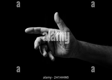 Schwarz-Weiß-Bild mit faltiger männlicher Hand, die mit offener Handfläche nach außen zeigt, isoliert vor einem schwarzen Hintergrund mit dramatischer Beleuchtung. Stockfoto