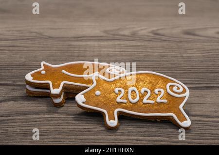 Niedliche Lebkuchenferkel für glückliches Neujahr 2022 auf einem braunen Holzhintergrund gestapelt. Nahaufnahme von goldgebackenen verzierten Plätzchen - Schweinchen für Viel Glück.