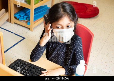 Bildung Preschool 4-5 Yar olds Mädchen, das alleine im Familienbereich spielt, mit dem Telefon spielt, es ans Ohr hält, während sie mit der Computertastatur spielt Stockfoto