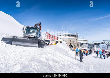 Zakopane, Polen März 2019 Touristen besichtigen die Schotterpiste des Kasprowy Wierch mit mehreren Pistenraupen, die vor Ort geparkt sind, und Skiliften im Hintergrund Stockfoto