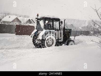 Bei starkem Schneefall räumt der Traktor die schneebedeckte Straße ab. Stockfoto